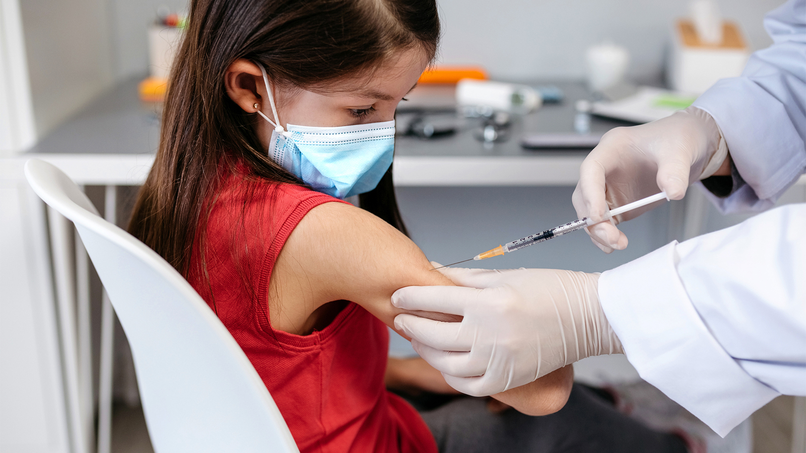 A young girl wearing a protective mask receives the COVID-19 vaccine