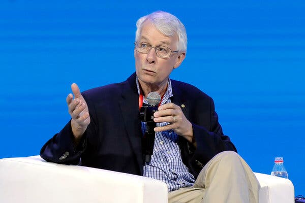 Richard Roberts wears a dark jacket over a striped shirt and khaki pants, as he holds a microphone during an onstage talk in 2019.