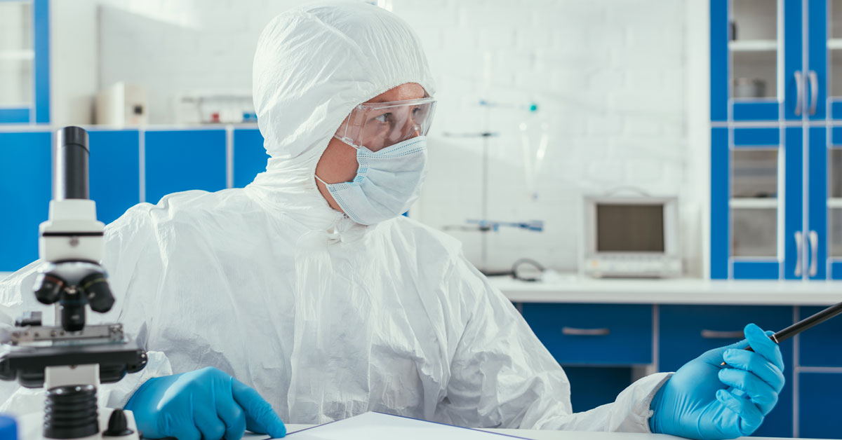 Biochemist in hazmat suit sitting near microscope Biochemist in hazmat suit sitting near microscope